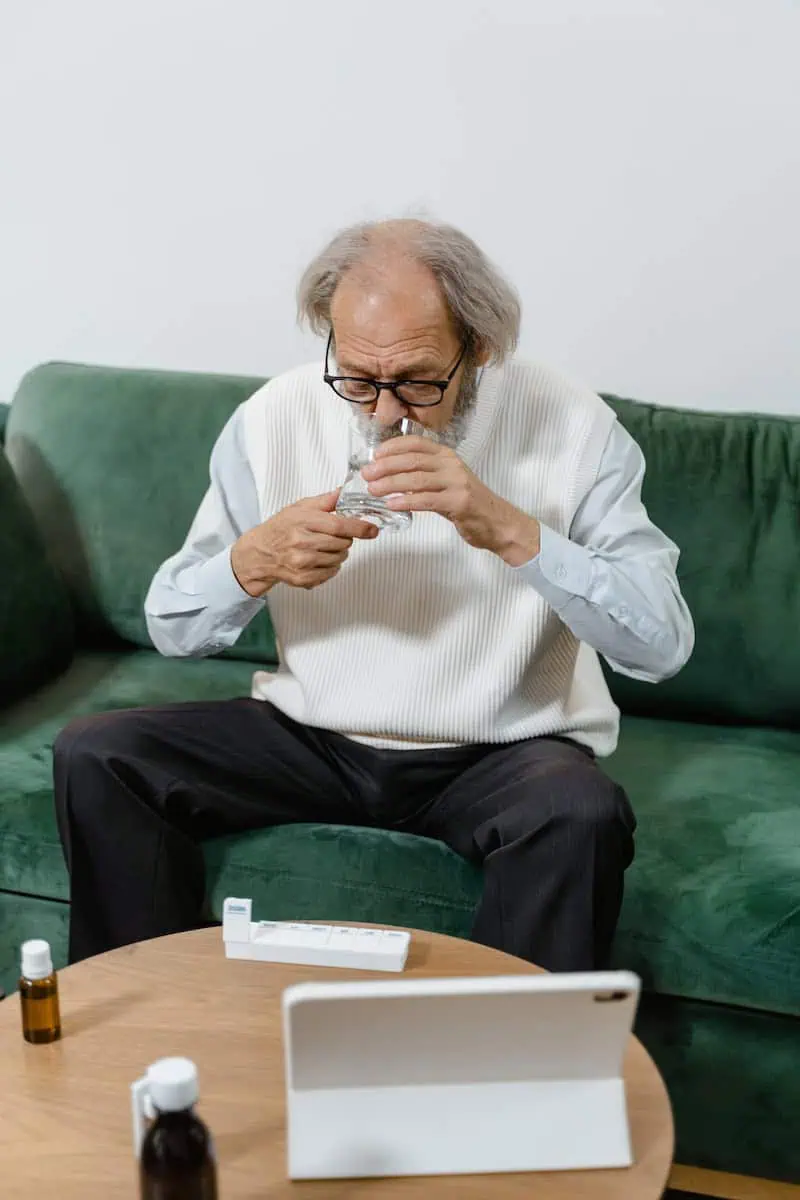 Elderly Man Taking His Medicine while Sitting on Green Couch