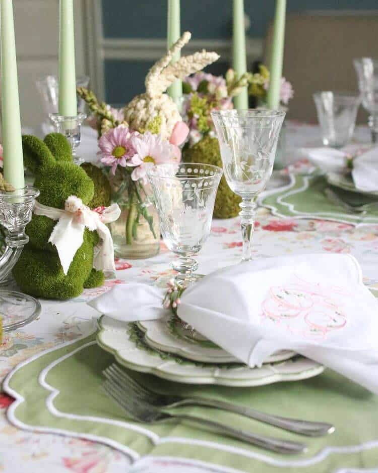Easter Tablescape ideas, Floral tablecloth with green placemats, white and green dishes with a white and pink embroidered napkin. Bunnies, flowers and candle centerpiece.