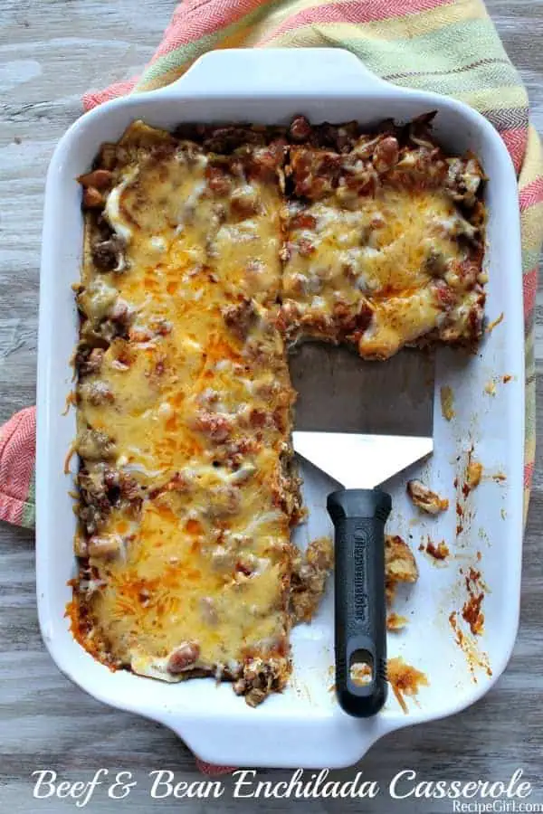 Beef and Bean Enchilada Casserole in a white baking dish, with a serving spoon- a cheap dinner 
