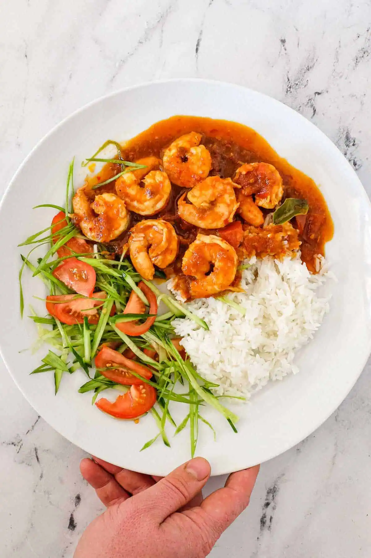 Sambal shrimp with rice and sliced tomatoes on a white plate.