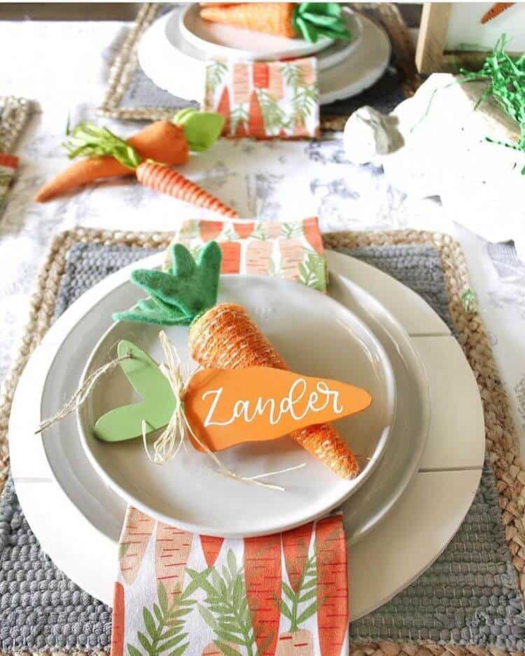 Creative Easter place card with name painted in a wood carrot. Carrot napkins and woven grey place mats, grey dishes and white chargers.