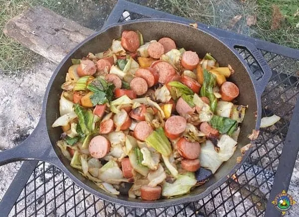 kielbasa and cabbage in a skillet over a campfire