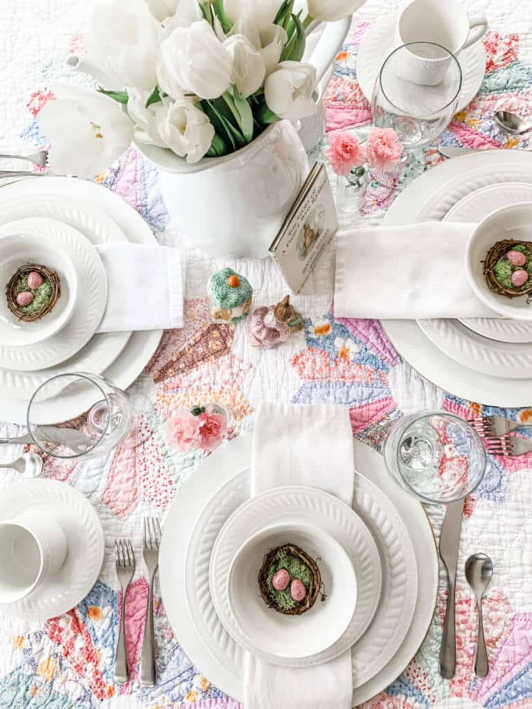 Vintage pink and blue quilt as tablecloth, white dishes layered with white napkins, egg nest at each plce settng, white tulip centerpiece.