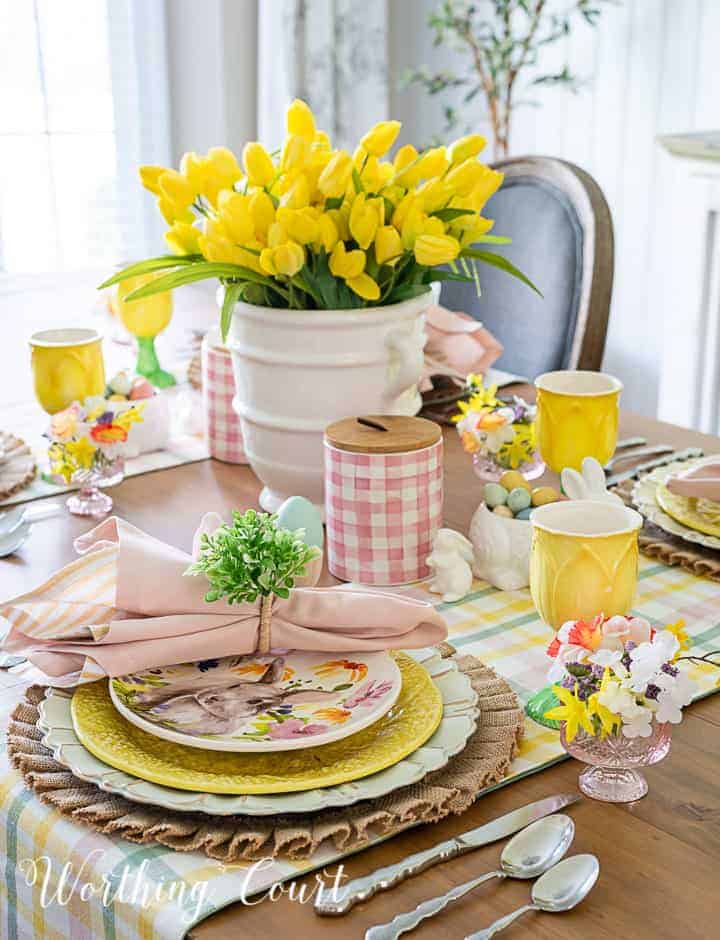Easter table set with yellow and floral and bunny plates, yellow tlip centerpiece.