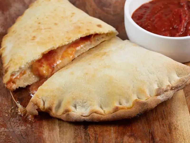 image 2611 - If your go-to dish is pizza, you might just be missing out on the magic of Classic Calzones. With soft fluffy dough wrapped around two kinds of melty cheese and warm pizza sauce, Classic Calzones are a pillowy pick-me-up meal. Filled with spicy, savory pepperoni, these calzones are hearty and heavenly. Make these Classic Calzones for a crowd or save them in the freezer for a quick grab-and-go meal.